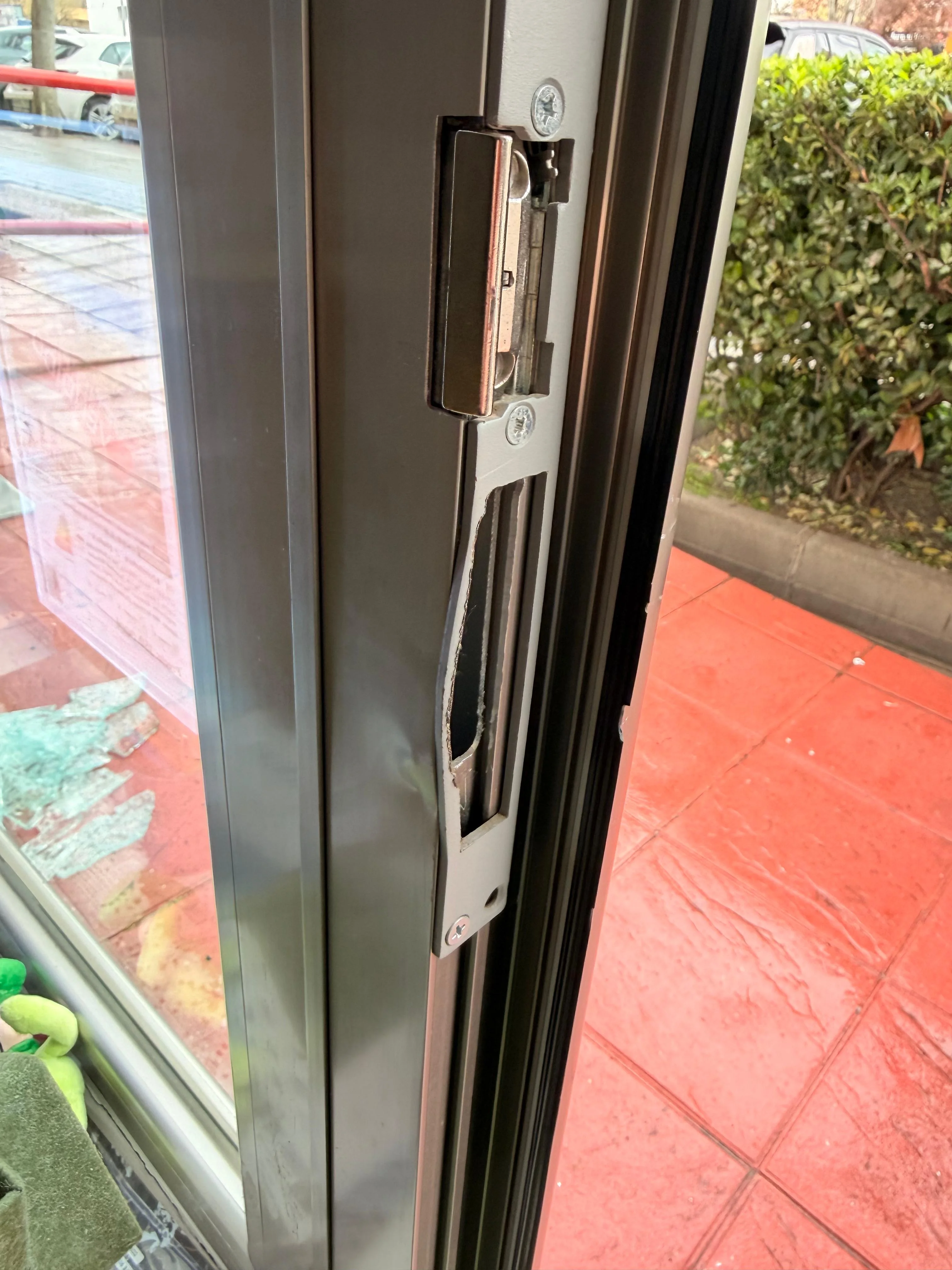 Antes (interior, ángulo): marco de la puerta de cristal con cerradero/chapa del cierre doblados hacia dentro